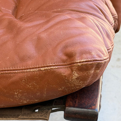 Close-up of a worn brown leather cushion with creases and scuffs, resting on dark wood—capturing the vintage charm of the Signature Vintage Ingmar Relling Siesta Set: two lounge chairs & rare coffee table.