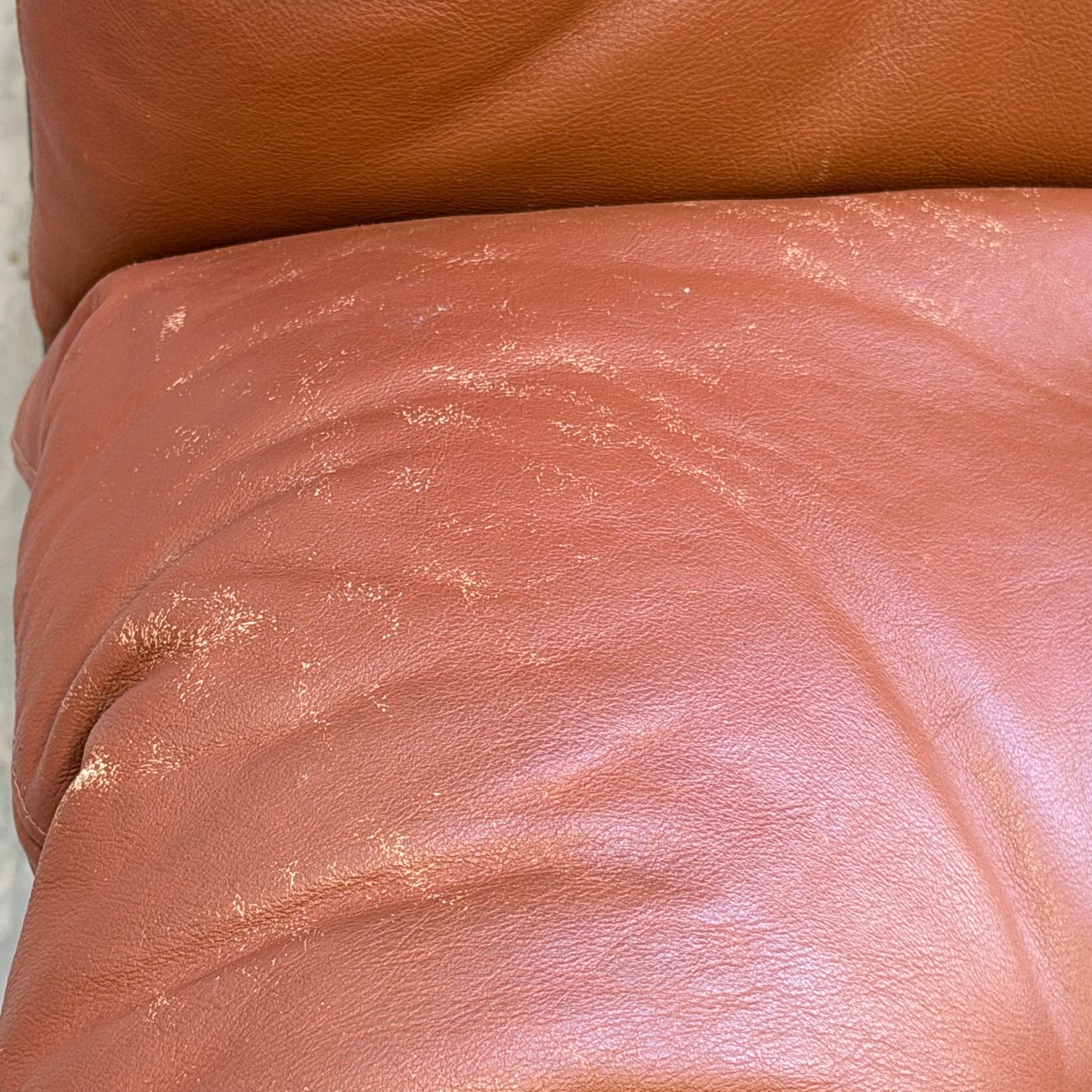 A close-up of a worn, reddish-brown leather cushion from the Signature Vintage Ingmar Relling Siesta Set—two lounge chairs & rare coffee table—with visible scuffs and faded areas adds character to this iconic mid-century Scandinavian design.