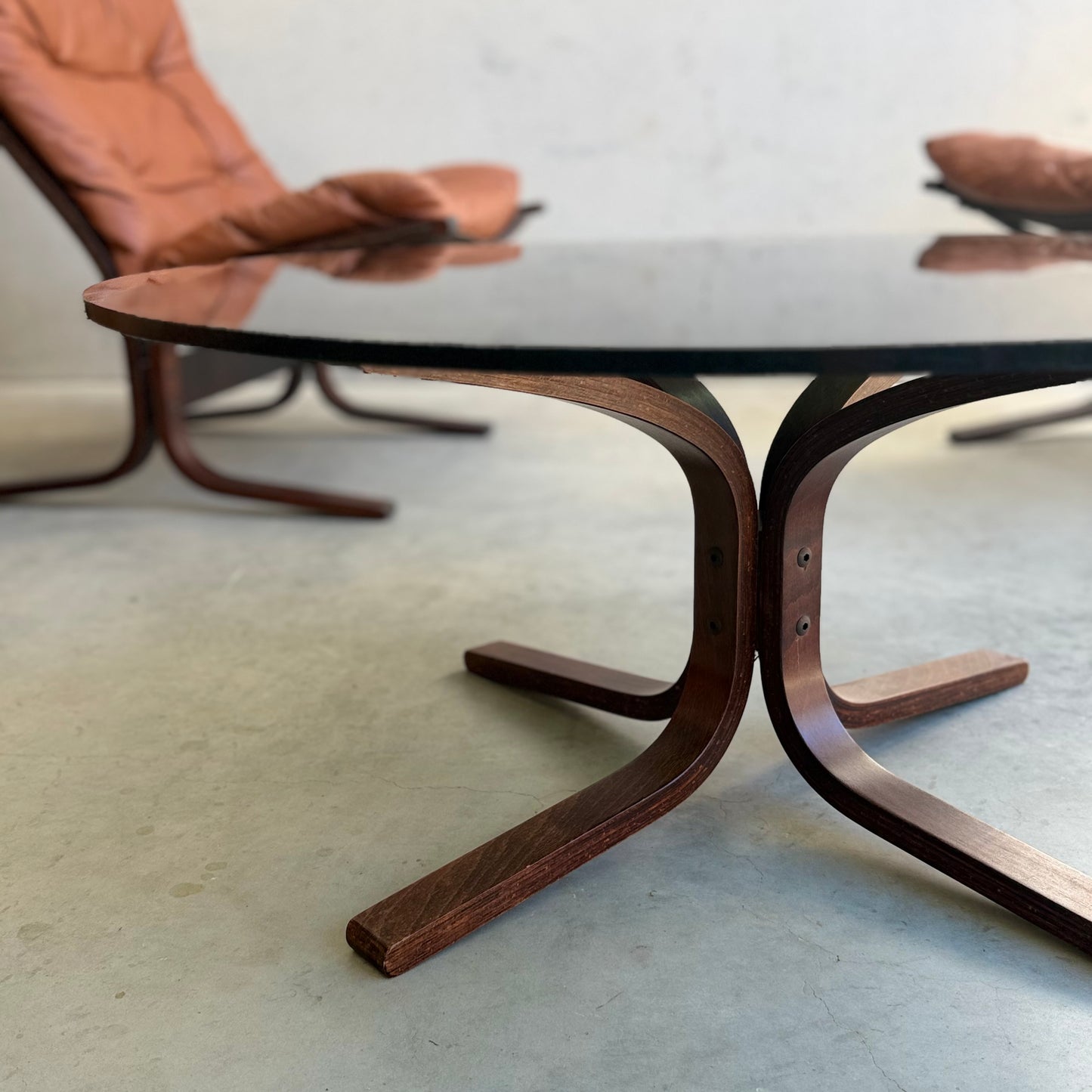 Close-up of the Signature Vintage Ingmar Relling Siesta Set featuring two lounge chairs and a rare glass-top coffee table with a curved wooden base, set on a light floor against a plain wall.