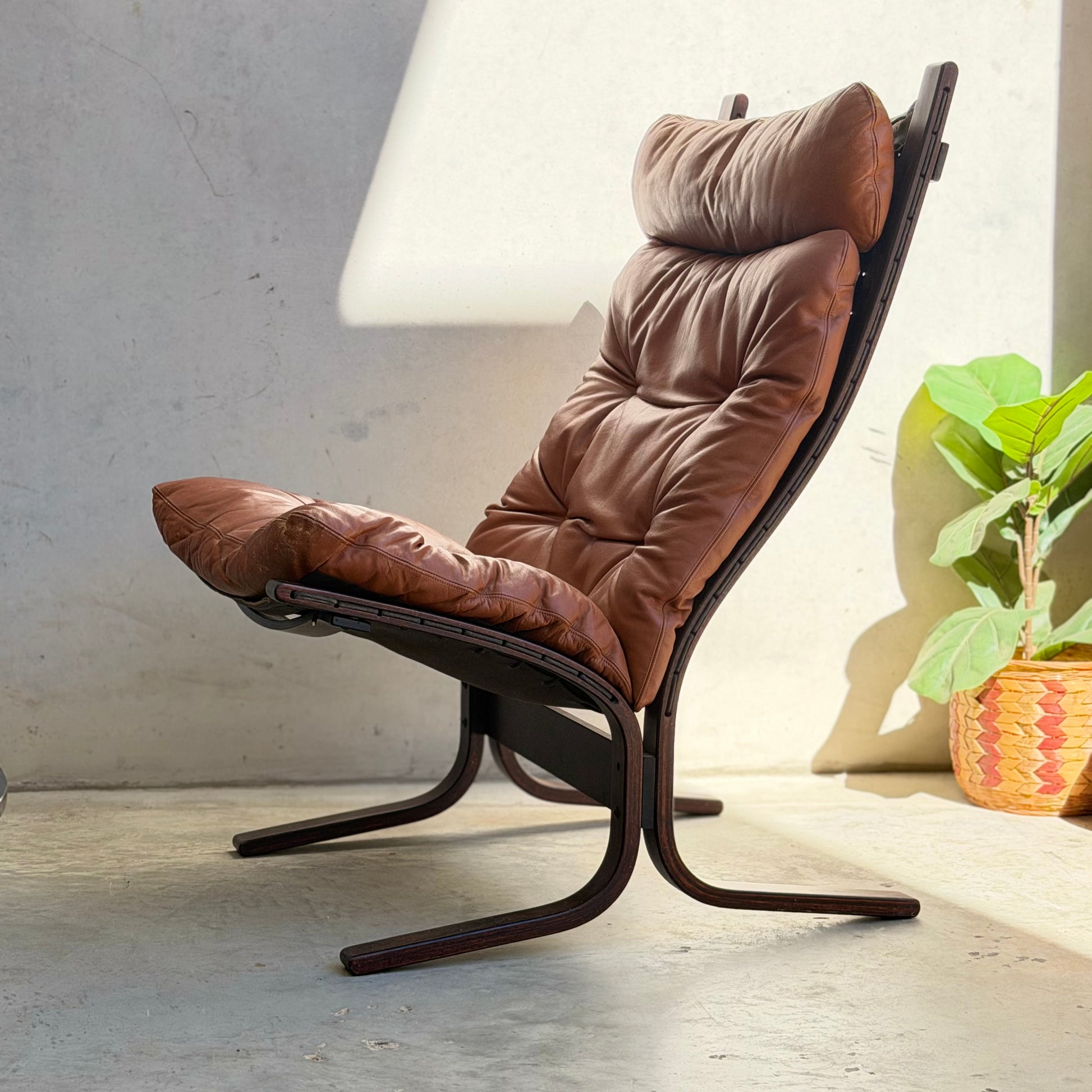 The Signature Vintage Ingmar Relling Siesta Set—two lounge chairs and a rare coffee table—features curved wooden frames and brown leather, highlighting classic Scandinavian mid-century design in a bright space with a concrete floor and greenery.