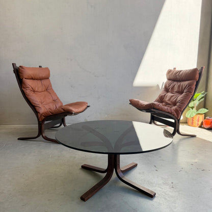The Signature Vintage Ingmar Relling Siesta Set features two lounge chairs facing each other with a rare round coffee table between them. Sunlight brightens the scene, while a small plant in an orange pot brings mid-century Scandinavian style.