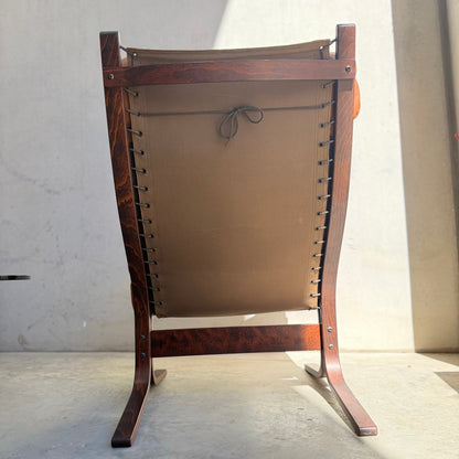 Viewed from behind, sunlight highlights the curved legs of the Signature Vintage Ingmar Relling Siesta Set—two lounge chairs with wooden frames and brown canvas backs, iconic of Scandinavian mid-century design.