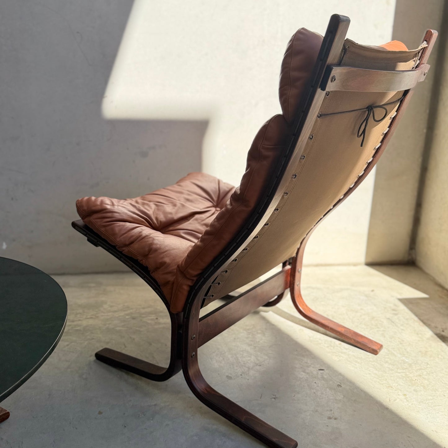 The Signature Vintage Ingmar Relling Siesta Set—two lounge chairs with brown leather cushions and wood frames plus a rare coffee table—captures Scandinavian mid-century style in sunlight near a light wall and dark round table.