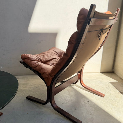 The Signature Vintage Ingmar Relling Siesta Set—two lounge chairs with brown leather cushions and wood frames plus a rare coffee table—captures Scandinavian mid-century style in sunlight near a light wall and dark round table.