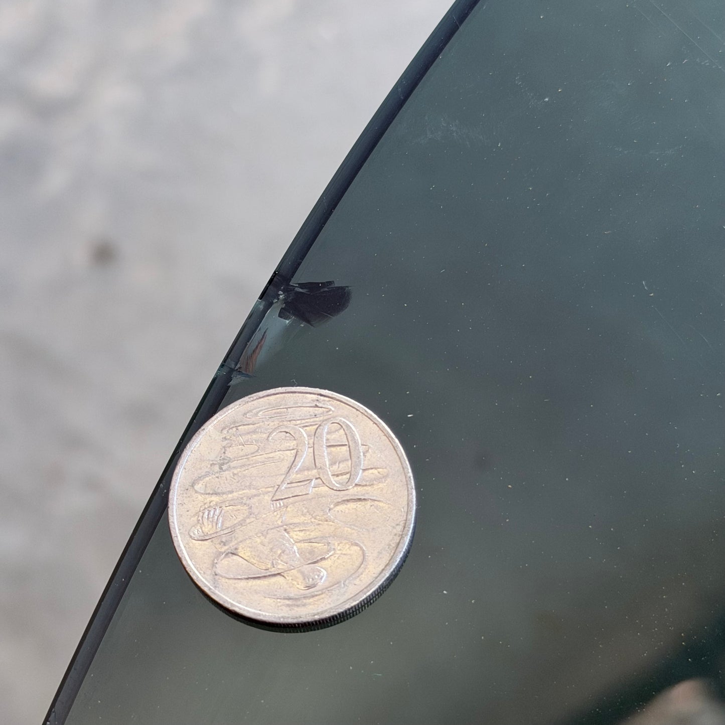 A 20-cent coin beside a small crack on a windshield provides scale, much like the precise detail found in the Signature Vintage Ingmar Relling Siesta Set – Two Lounge Chairs & Rare Coffee Table.