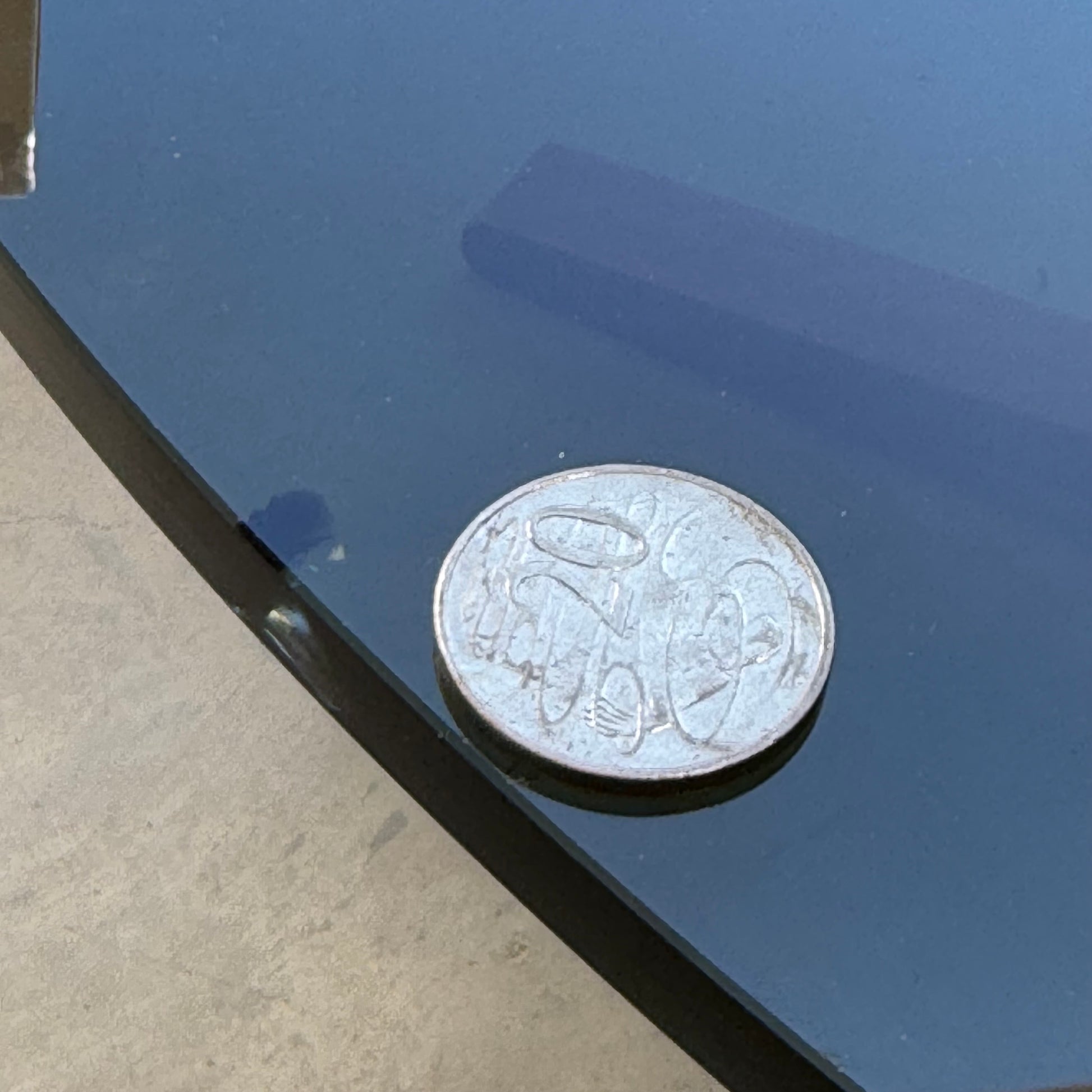 A close-up of a 50 cent coin on glass reflects the sleek lines of Scandinavian mid-century style, with the Signature Vintage Ingmar Relling Siesta Set—two lounge chairs and rare coffee table—on a concrete floor in the background.