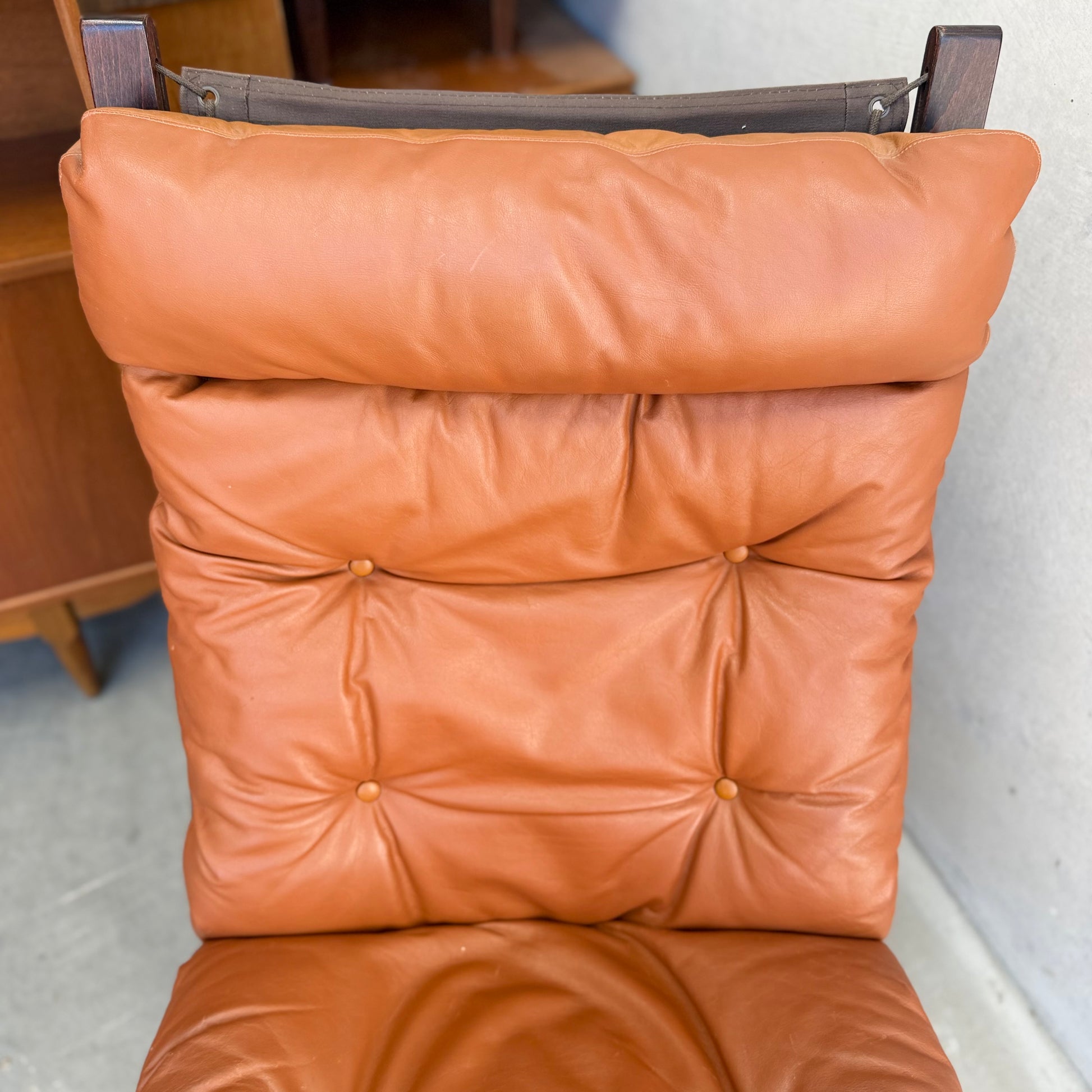 A close-up of the Signature Vintage Ingmar Relling Siesta Set’s lounge chair, featuring caramel leather upholstery and wooden frame, highlights the cushioned backrest and seat reminiscent of iconic mid-century design.