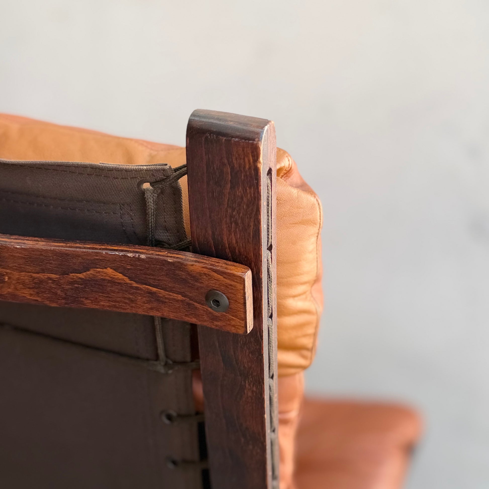 Close-up of the Signature Vintage Ingmar Relling Siesta Set: top corner of one lounge chair showing detailed wood grain, joinery, brown leather cushions, and fabric backing—all against a plain, light-colored background.