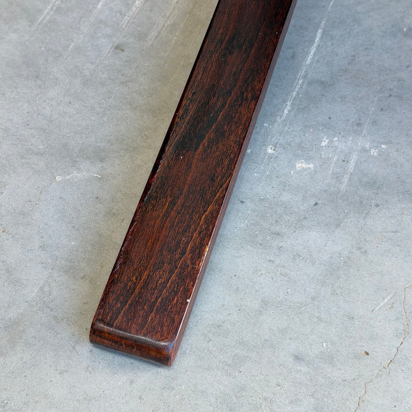 A close-up of the Signature Vintage Ingmar Relling Siesta Set’s dark wood coffee table leg resting on a textured light gray concrete floor, echoing the iconic style of the included lounge chairs.