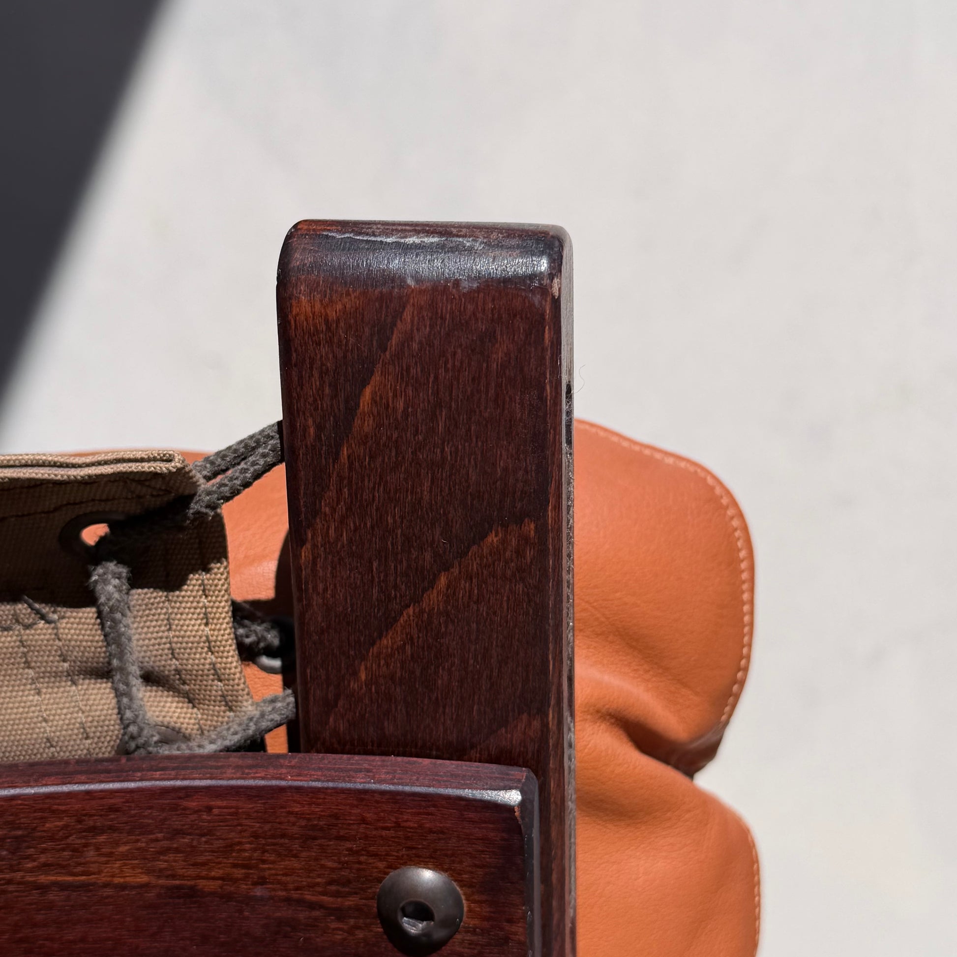 Close-up of a Signature Vintage Ingmar Relling Siesta Set armrest—showing brown finish, tan leather cushion, and beige fabric drawstrings—iconic Scandinavian design from two lounge chairs & rare coffee table, set against a blurred backdrop.