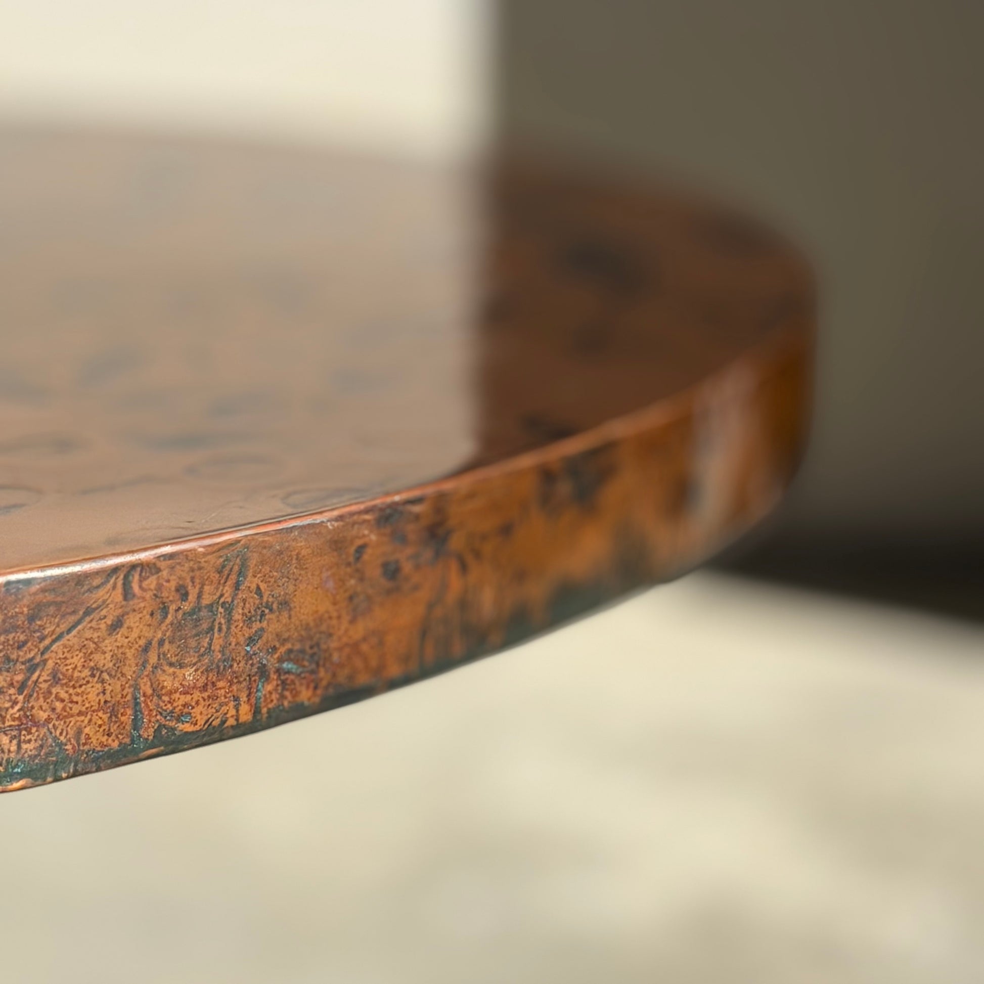 Close-up of the Vintage Louis Berczi Hammered Copper Round Coffee Table—Rare Australian Collectible (Revive)—showing its hand-hammered, shiny copper edge with a blurred background to highlight its unique texture and craftsmanship.