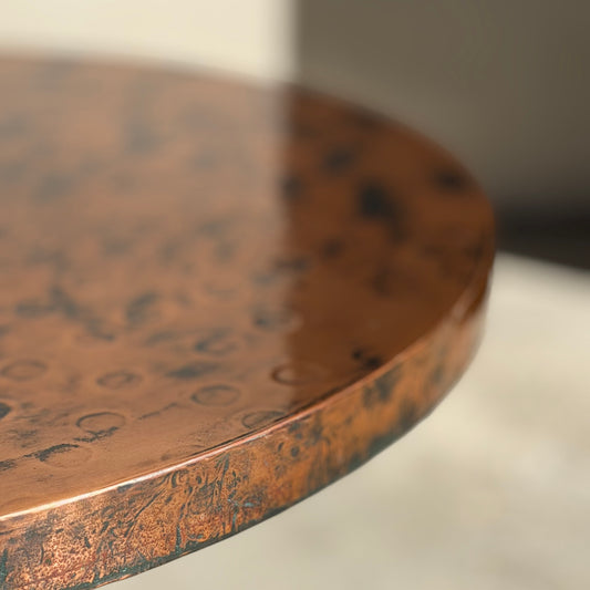 Close-up of the edge of the Vintage Louis Berczi Hammered Copper Round Coffee Table—Rare Australian Collectible—showing its hand-hammered, textured copper surface reflecting light against a softly blurred, neutral background.