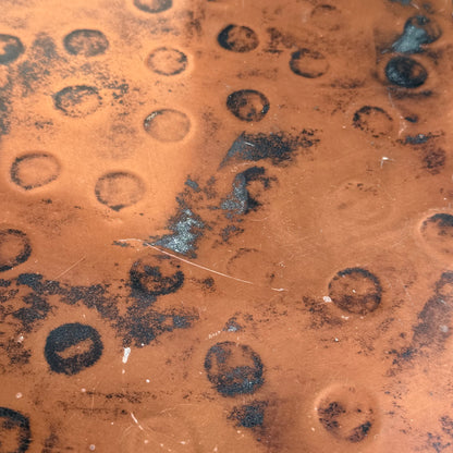 Close-up of a textured, weathered surface with rusty orange tones, black marks, and dark patches—echoing the artistry of the Vintage Louis Berczi Hammered Copper Round Coffee Table – Rare Australian Collectible (Revive).