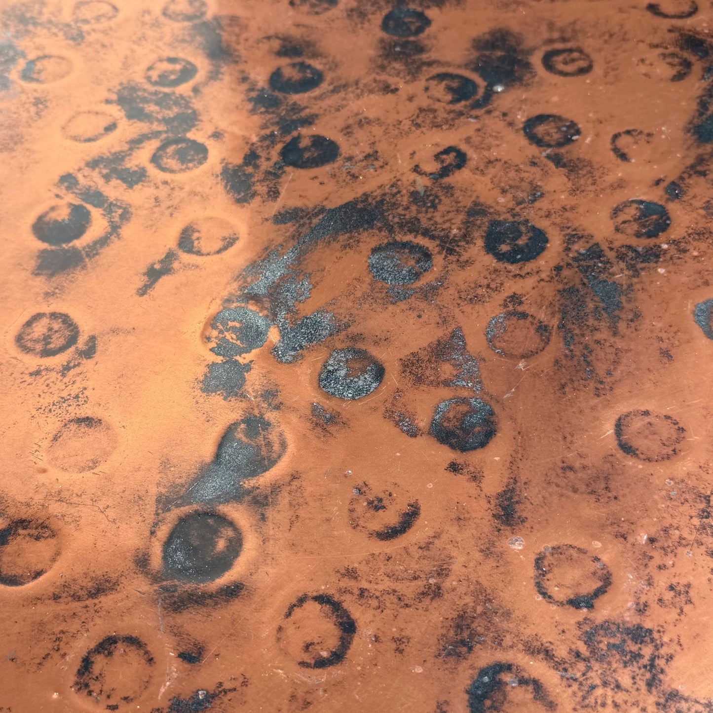 Close-up of a textured, orange-brown surface with black marks and circular indentations—evoking the Vintage Louis Berczi Hammered Copper Round Coffee Table, a rare Australian collectible with an industrial, hand-hammered copper finish.