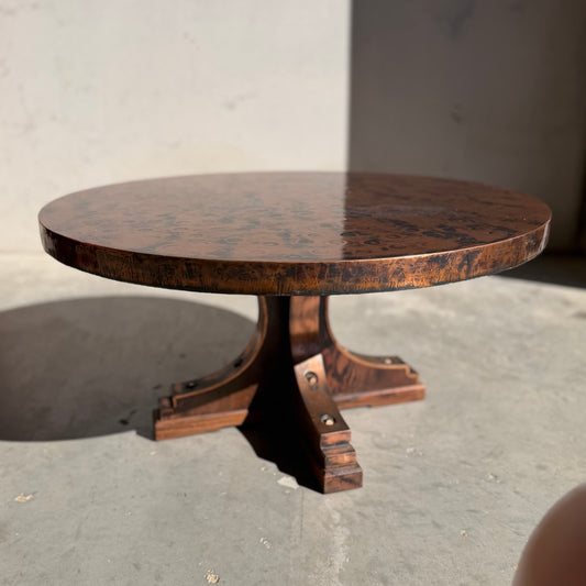 A rare Vintage Louis Berczi Hammered Copper Round Coffee Table (Revive) with a polished top and pedestal base sits on a concrete floor, sunlight casting shadows—an Australian collectible.