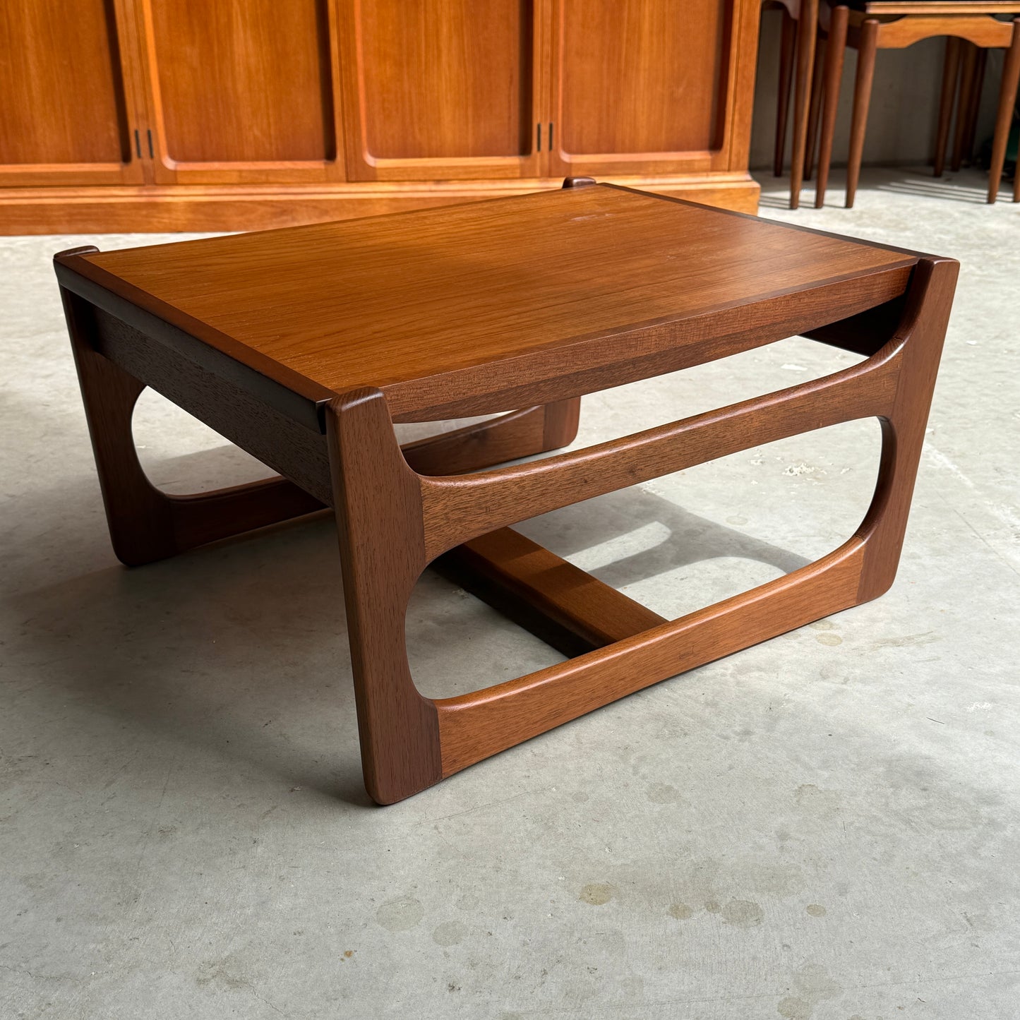 An ultra rare Gerald Easden Coffee Table in Blackwood with a sleigh leg base (Rediscover) sits on a concrete floor in front of wood-paneled cabinets—an elegant nod to Australian vintage furniture.