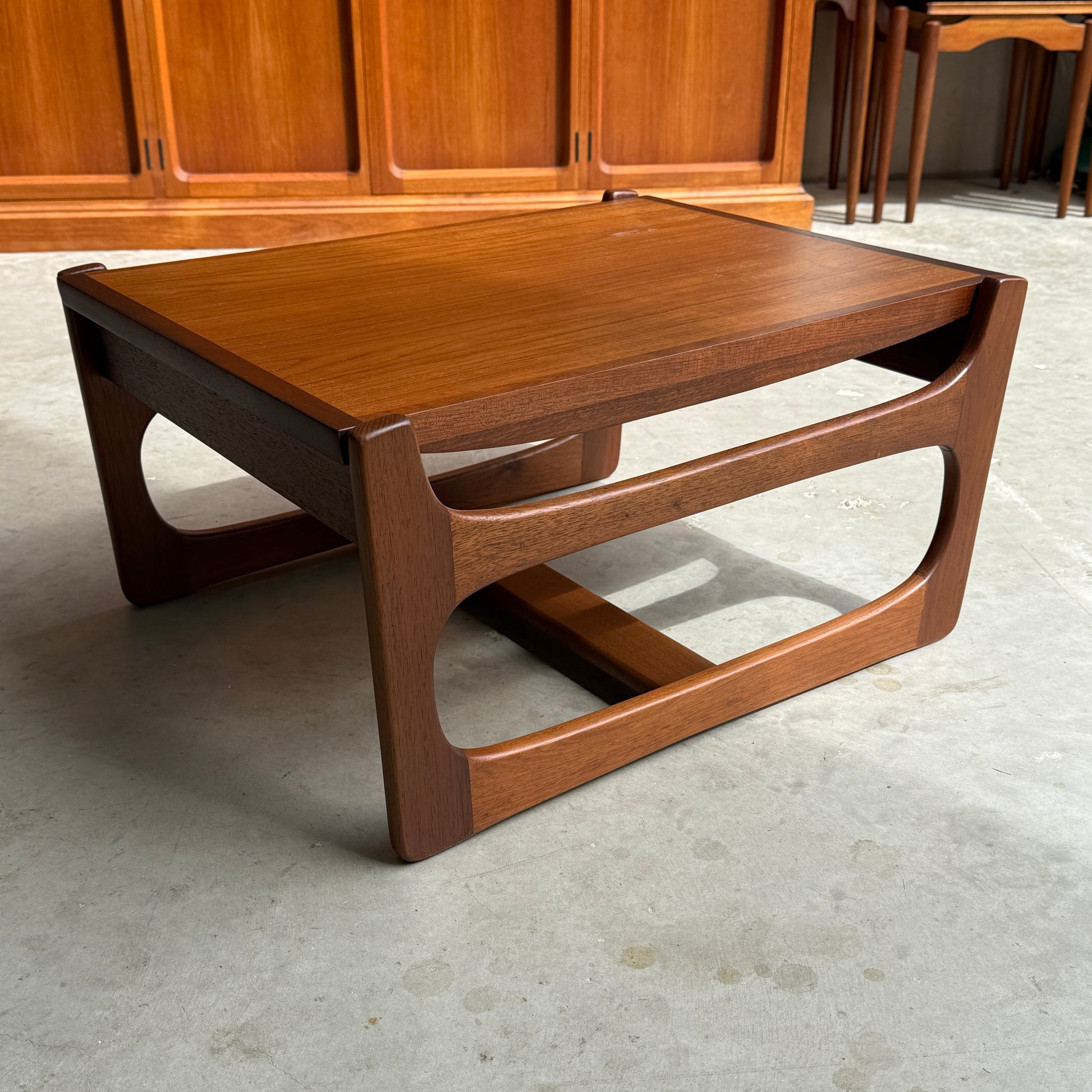 An ultra rare Gerald Easden Coffee Table in Blackwood with a sleigh leg base (Rediscover) sits on a concrete floor in front of wood-paneled cabinets—an elegant nod to Australian vintage furniture.