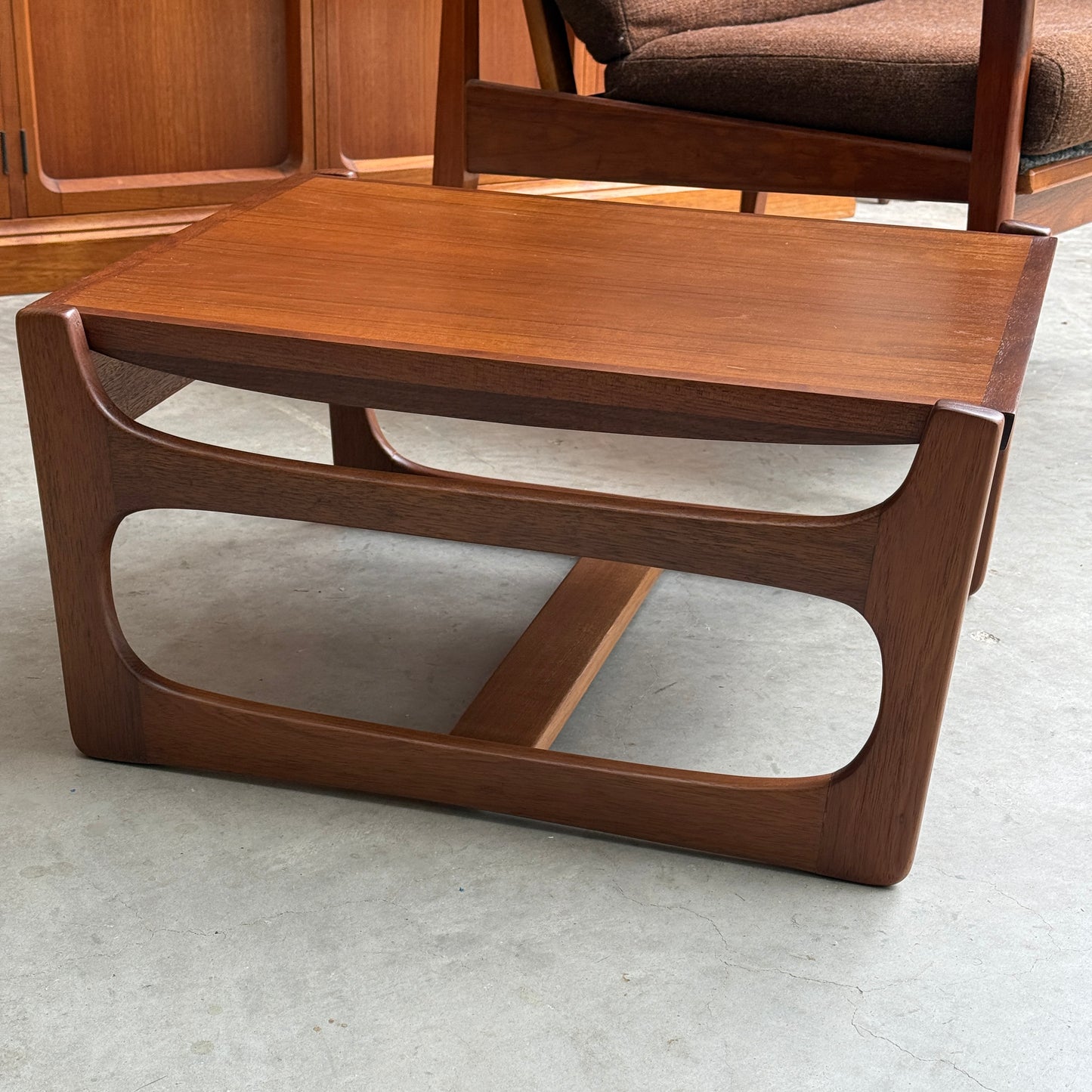 An ultra rare Gerald Easden coffee table in Blackwood with a sleigh leg base (Rediscover) sits on a concrete floor, showcasing mid-century style. A brown upholstered chair is partially visible behind this unique piece of Australian vintage furniture.