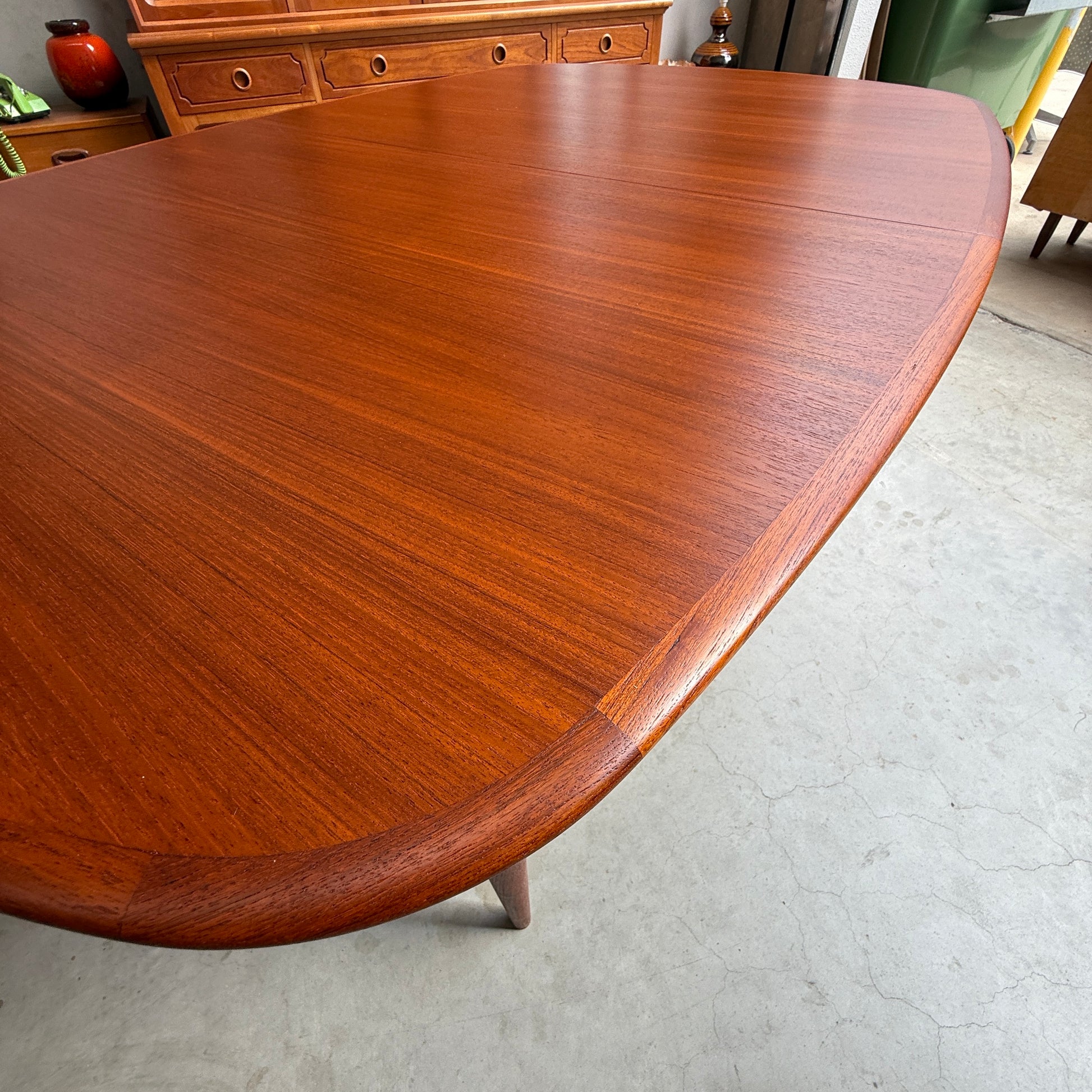 A close-up of the Fully Restored Parker No.92 D End Dining Table (Rediscover) with rounded edges sits on a concrete floor, complemented by a matching sideboard and decor that showcase vintage Australian furniture charm in the background.