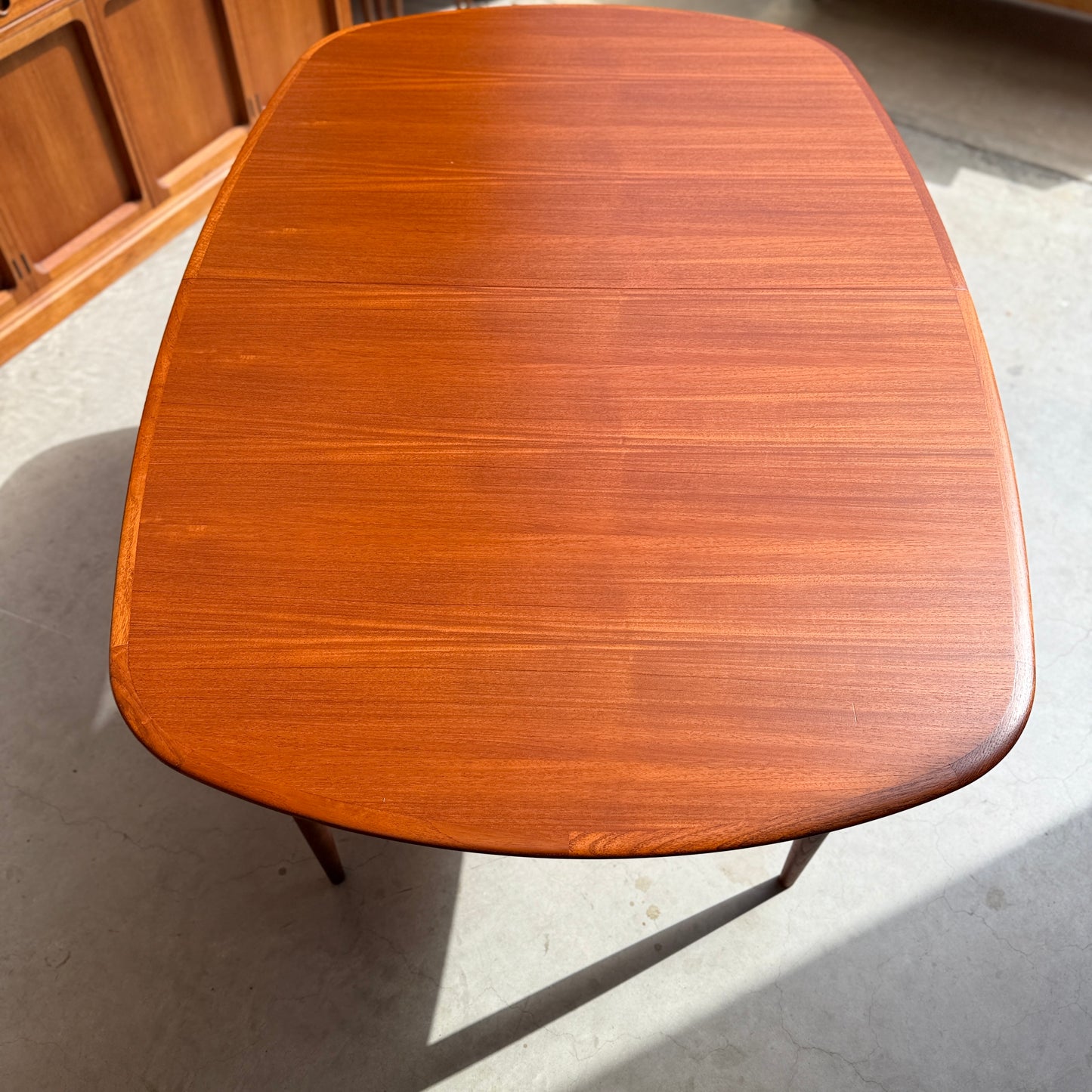 A Fully Restored Parker No.92 D End Dining Table (Rediscover) stands on a light floor in sunlight, with wooden cabinets behind it, showcasing classic mid-century modern style.