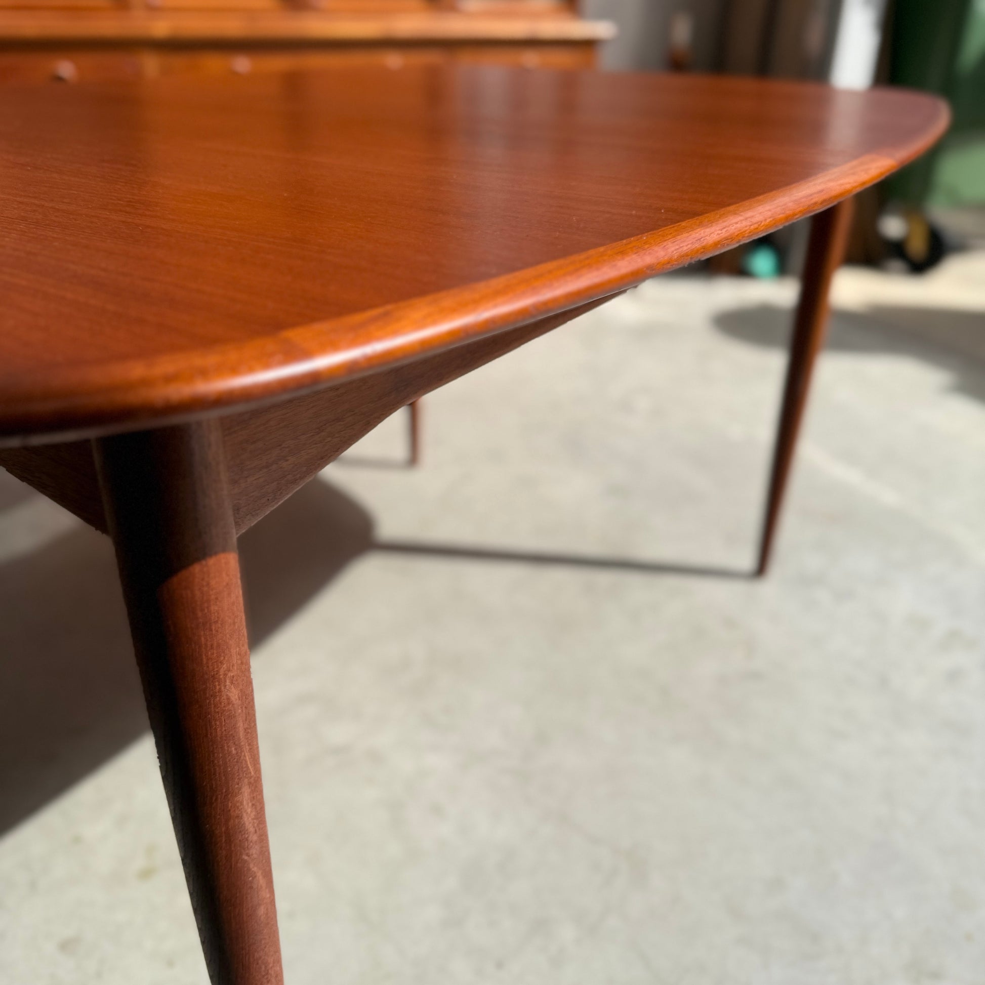 Close-up of the Fully Restored Parker No.92 D End Dining Table (Rediscover), showing its tapered legs on a sunlit concrete floor, with smooth curved edges and warm wood grain highlighting its mid-century Australian vintage style.
