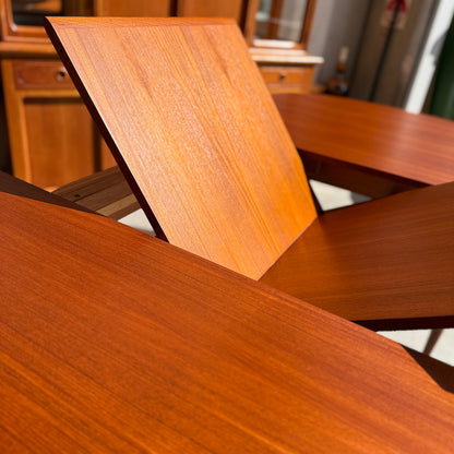 Close-up of the Fully Restored Parker No.92 D End Dining Table (Rediscover) with its extension leaf being unfolded, highlighting the mechanism and rich wood grain. Blurred mid-century modern cabinets and furniture can be seen in the background.