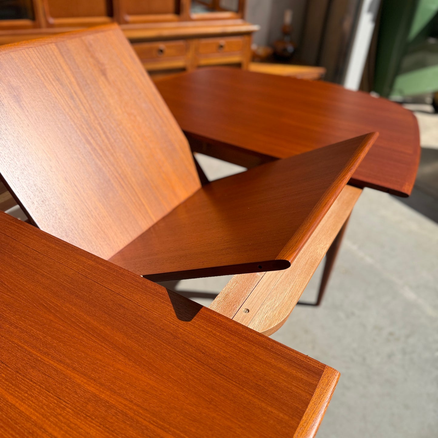 Fully restored Parker No.92 D End Dining Table (Rediscover) with extending leaves and a rich finish, sunlit on a gray floor, paired with vintage Australian furniture in the background.