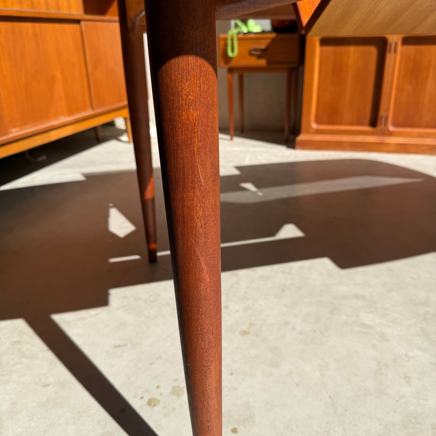 Close-up of the legs and shadow of a Fully Restored Parker No.92 D End Dining Table (Rediscover) on a sunlit concrete floor, with vintage Australian furniture and sunlight visible in the background.