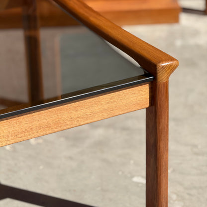 Close-up of a Tessa TC 21 Coffee Table Frame Restored - (Revive) with a glass top, smooth rounded edges, and warm brown wood grain, set on a concrete floor—ideal for fans of modern minimalist design.