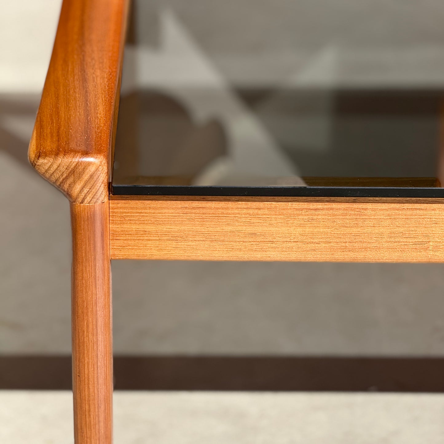 Close-up of the Tessa TC 21 Coffee Table Frame Restored (Revive) with a glass top, highlighting smooth joinery, natural wood grain, and modern minimalist craftsmanship as sunlight casts shadows below.