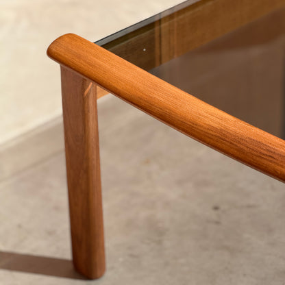 A close-up of the Tessa TC 21 Coffee Table Frame Restored (Revive) leg and edge, highlighting polished wood seamlessly joined with glass in a modern minimalist style, casting soft shadows on a light-colored floor.