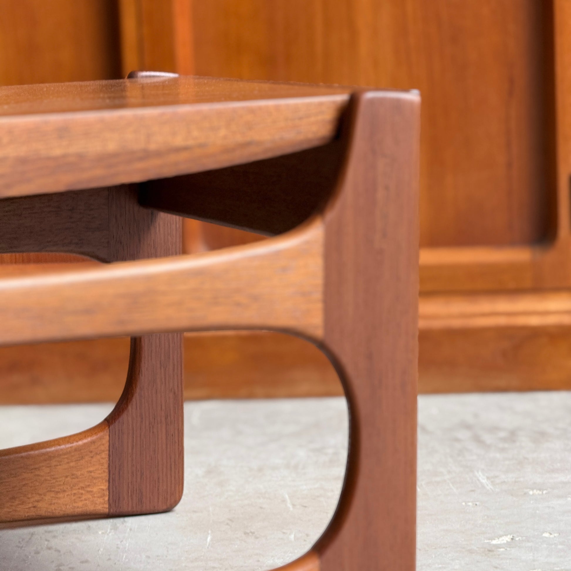 Close-up of the ultra rare Gerald Easden Coffee Table in Blackwood with a sleigh leg base, highlighting its elegant curved lines and mid-century modern design. The background shows matching wood paneling and a concrete floor.