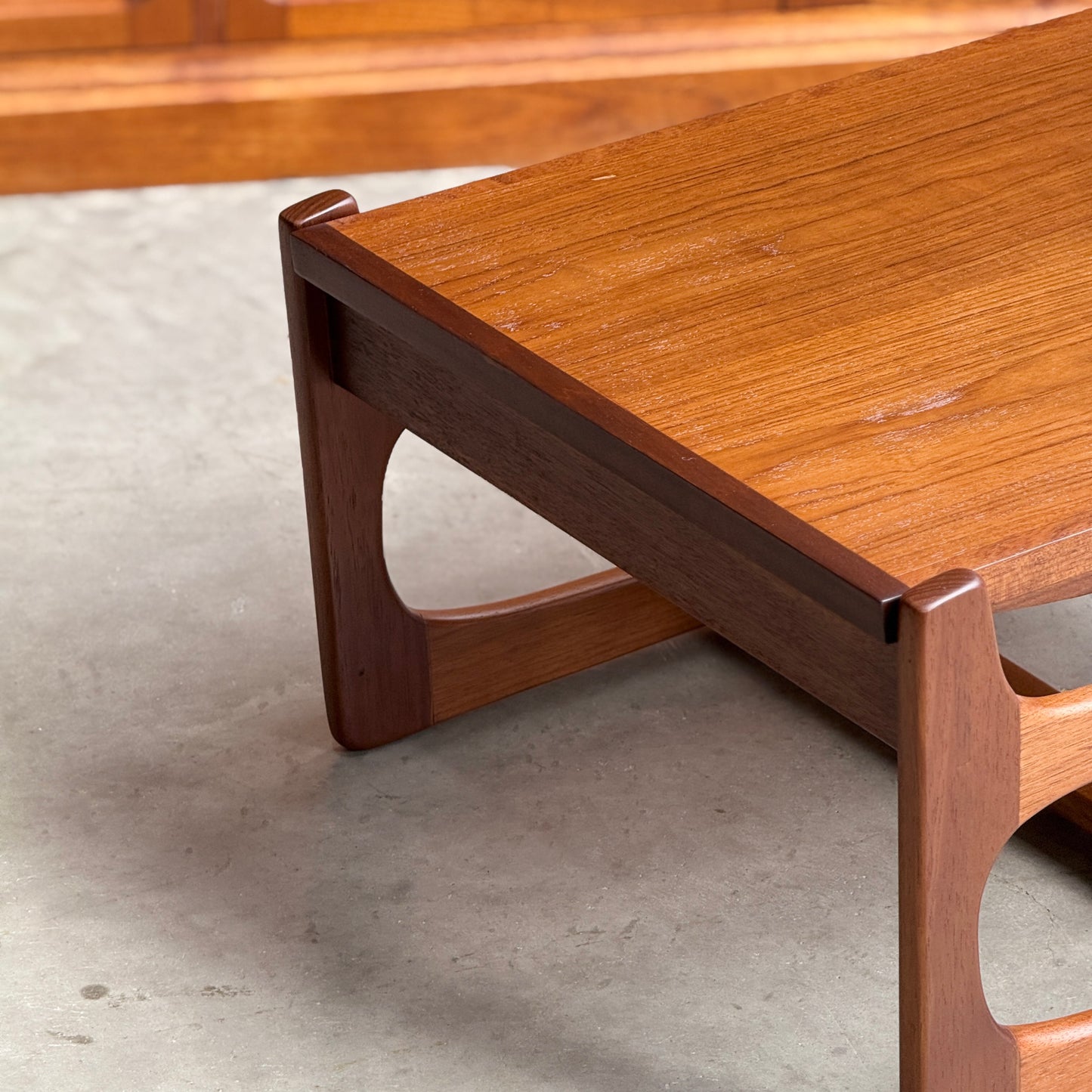 A close-up of the Ultra Rare Gerald Easden Coffee Table in Blackwood with a sleigh leg base (Rediscover), showcasing its mid-century modern design and smooth finish, set on a light gray concrete floor.