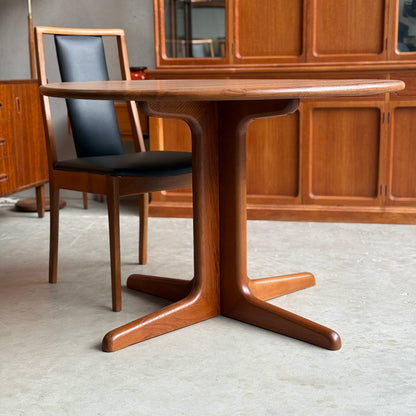 A Fully Restored Solid Teak Danish Dining Table (Rediscover) with a central pedestal base is paired with a black cushioned chair, complementing the room’s wooden cabinets.