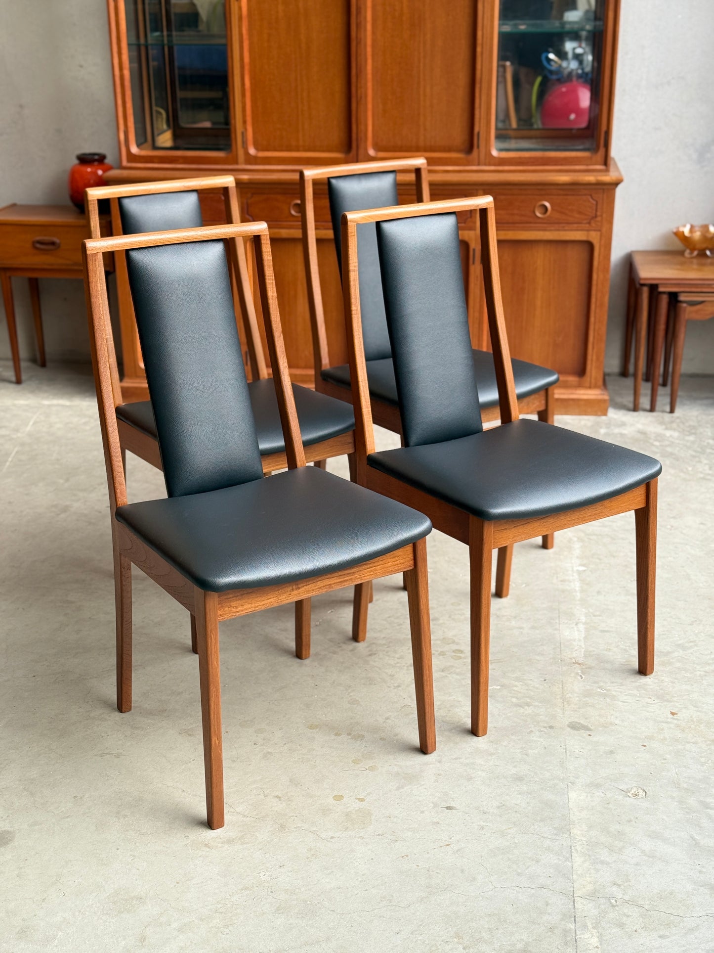 Mid century modern Noblett Dining chairs with black leather seats and wooden frames in a room with wooden furniture.