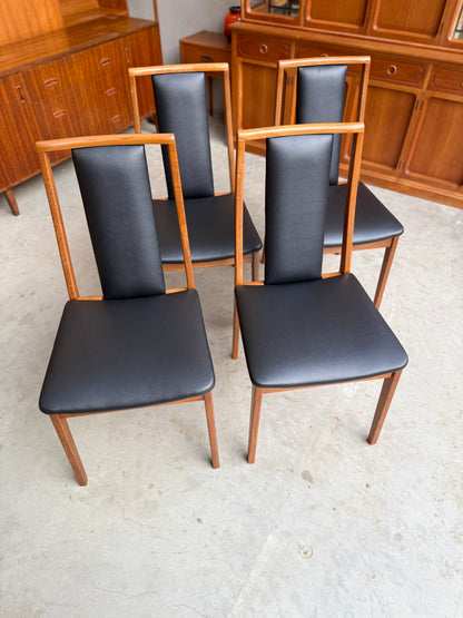 Mid Century Modern Noblett Four black chairs with wooden frames on a light-colored floor.