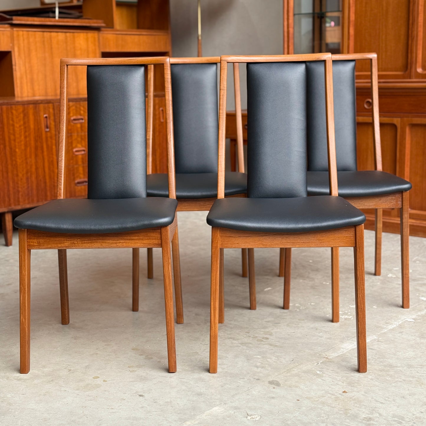 Four wooden chairs with black leather seats in a room with wooden furniture.