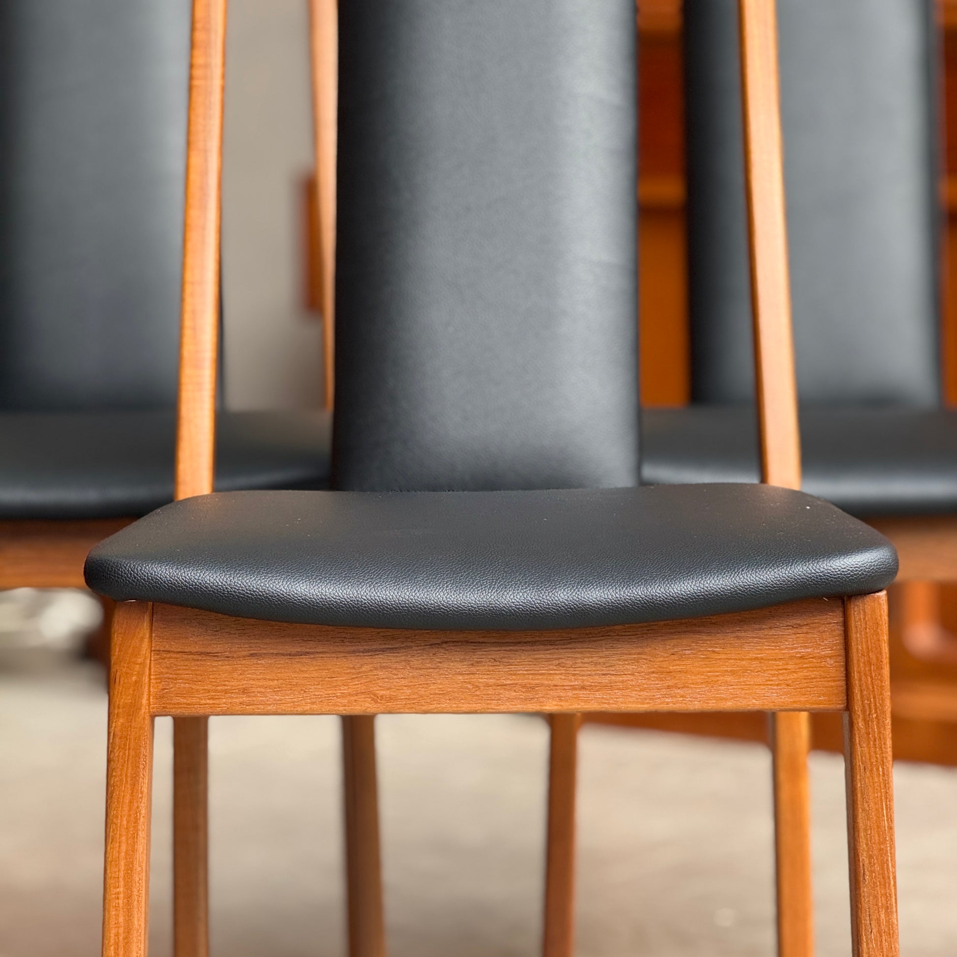 Close-up of a chair with black leather seat and wooden frame.