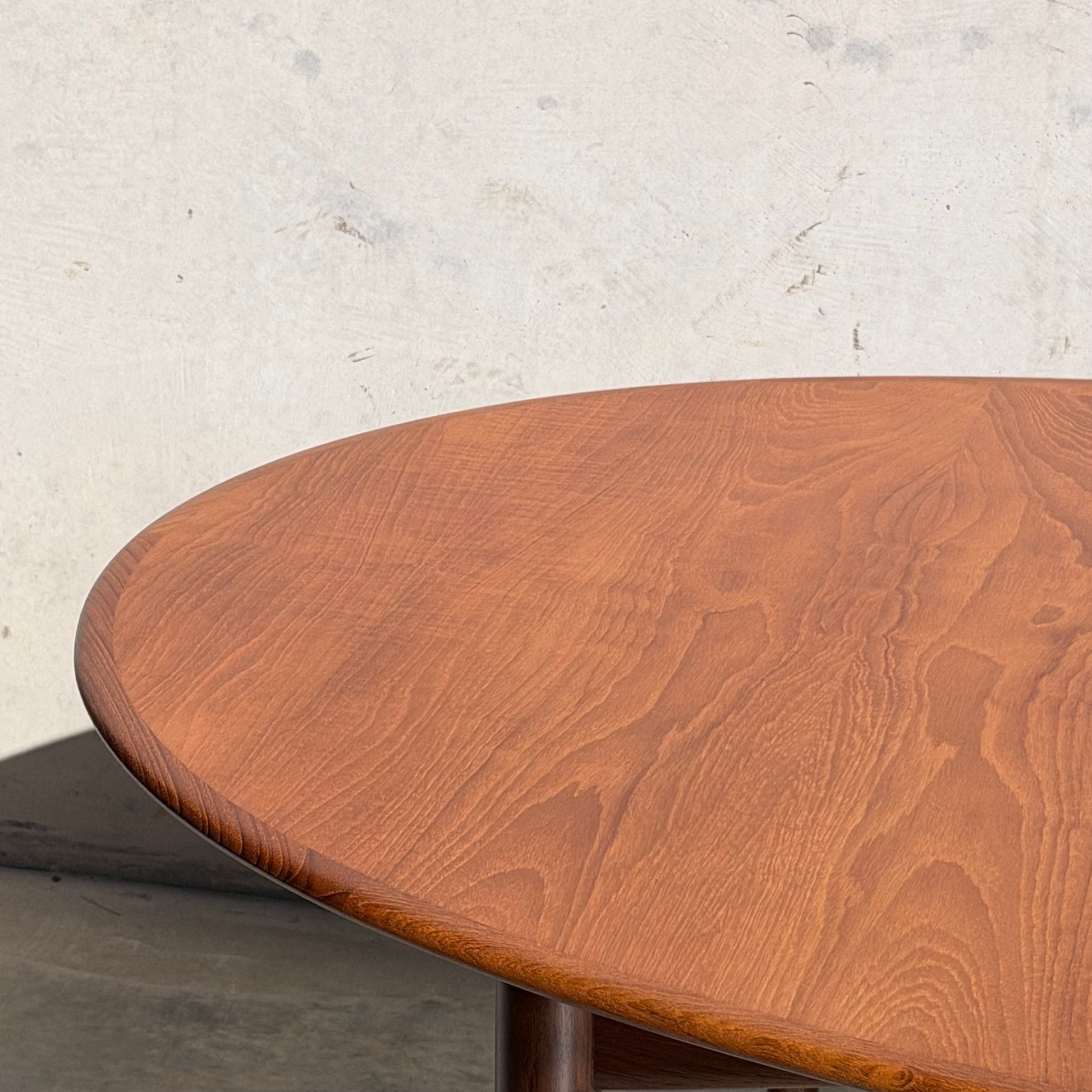 A close-up of the edge and surface of the Fully Restored Parker No.91 Fixed Top Oval Table (Rediscover), showcasing its warm brown finish against a plain, light-colored wall.