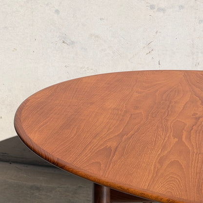 A close-up of the edge and surface of the Fully Restored Parker No.91 Fixed Top Oval Table (Rediscover), showcasing its warm brown finish against a plain, light-colored wall.