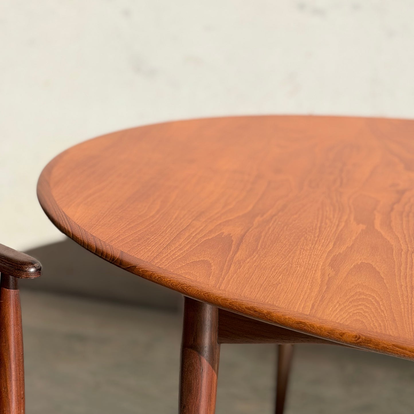 A close-up of a Fully Restored Parker No.91 Fixed Top Oval Table (Rediscover) showcases its grain patterns, paired with part of a matching wooden chair, set against a plain, light-colored background.