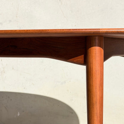 Close-up of the Fully Restored Parker No.91 Fixed Top Oval Table (Rediscover) corner with smooth, rounded edges and a cylindrical leg, sunlight casting shadows on its teak surface against a light wall.