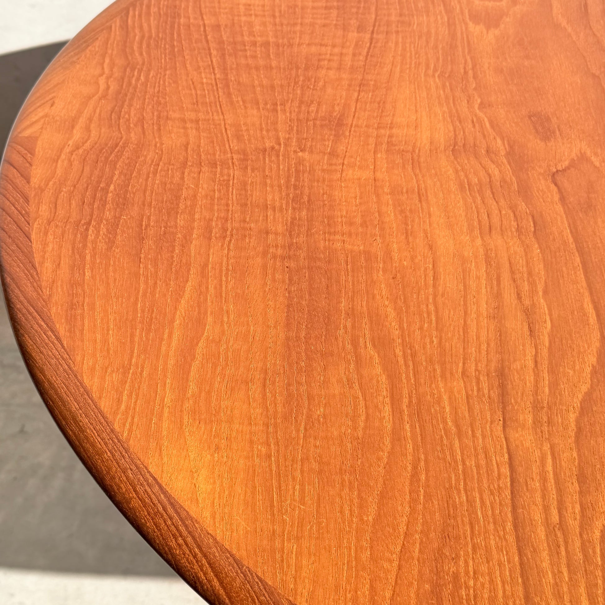 Close-up of the Fully Restored Parker No.91 Fixed Top Oval Table (Rediscover), featuring a smooth finish and visible natural grain, gently curving edge, and bathed in sunlight against a light-colored background.