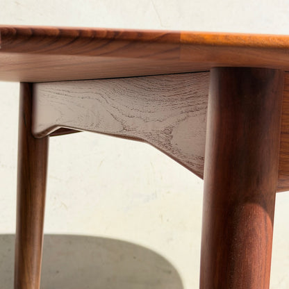 Close-up of a Fully Restored Parker No.91 Fixed Top Oval Table (Rediscover) corner, highlighting its smooth, rounded legs and natural wood grain finish as sunlight casts soft shadows on a light background.