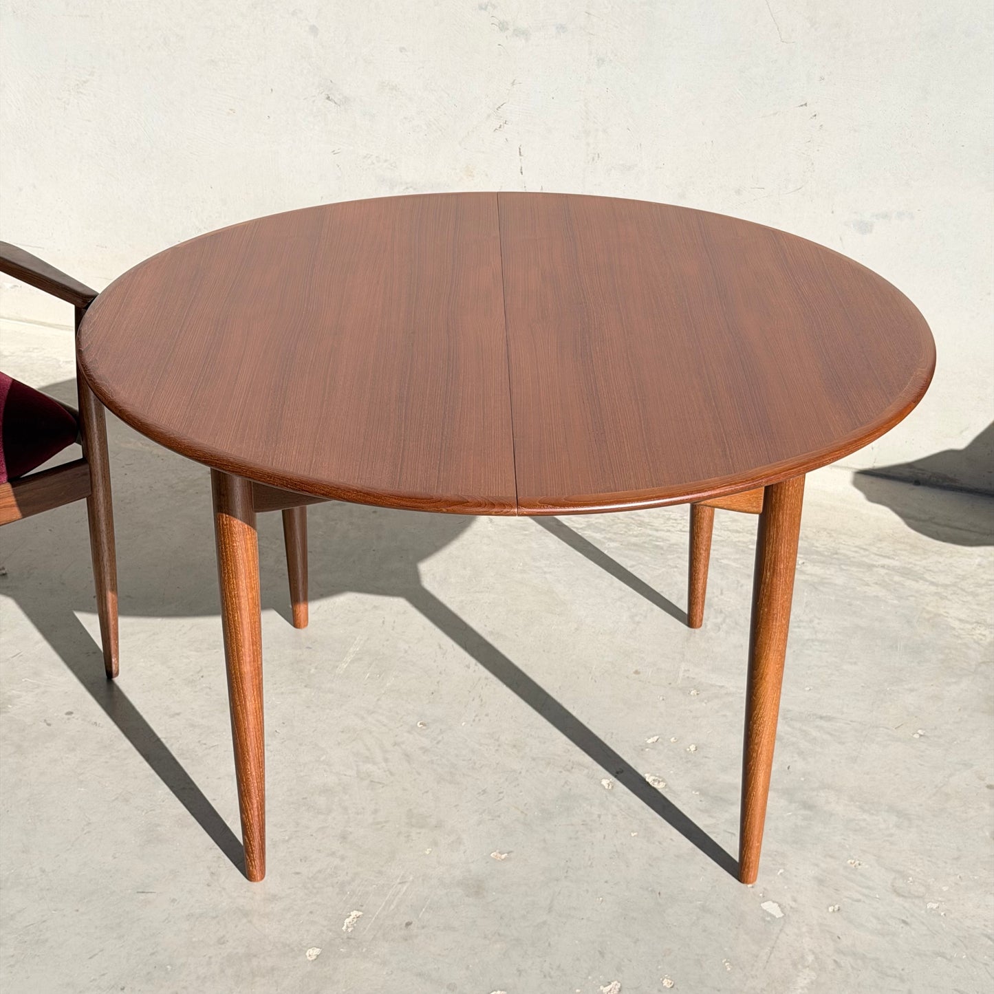 The Fully Restored Parker 90 Round Extension Butterfly Table Only (Rediscover), featuring four tapered legs and mid-century modern style, is shown on a light concrete surface with a wooden chair partially visible to the left.