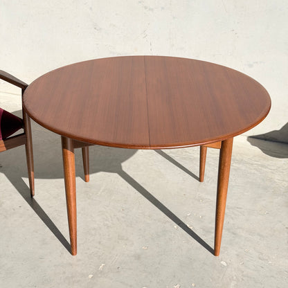The Fully Restored Parker 90 Round Extension Butterfly Table Only (Rediscover), featuring four tapered legs and mid-century modern style, is shown on a light concrete surface with a wooden chair partially visible to the left.