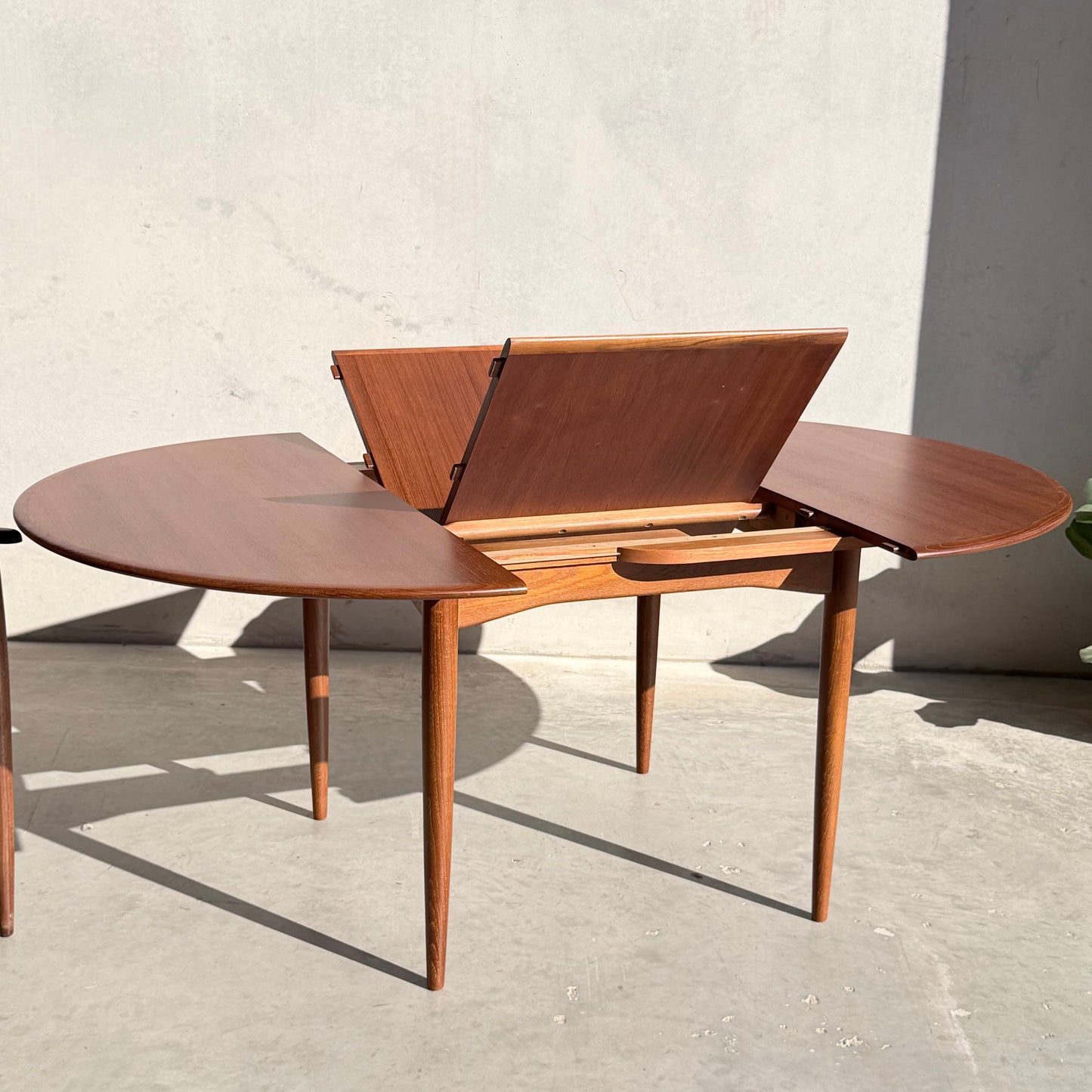 A fully restored Parker 90 Round Extension Butterfly Table Only (Rediscover), featuring a sleek mid-century design and extendable function, is set on a light floor against a plain, sunlit wall.