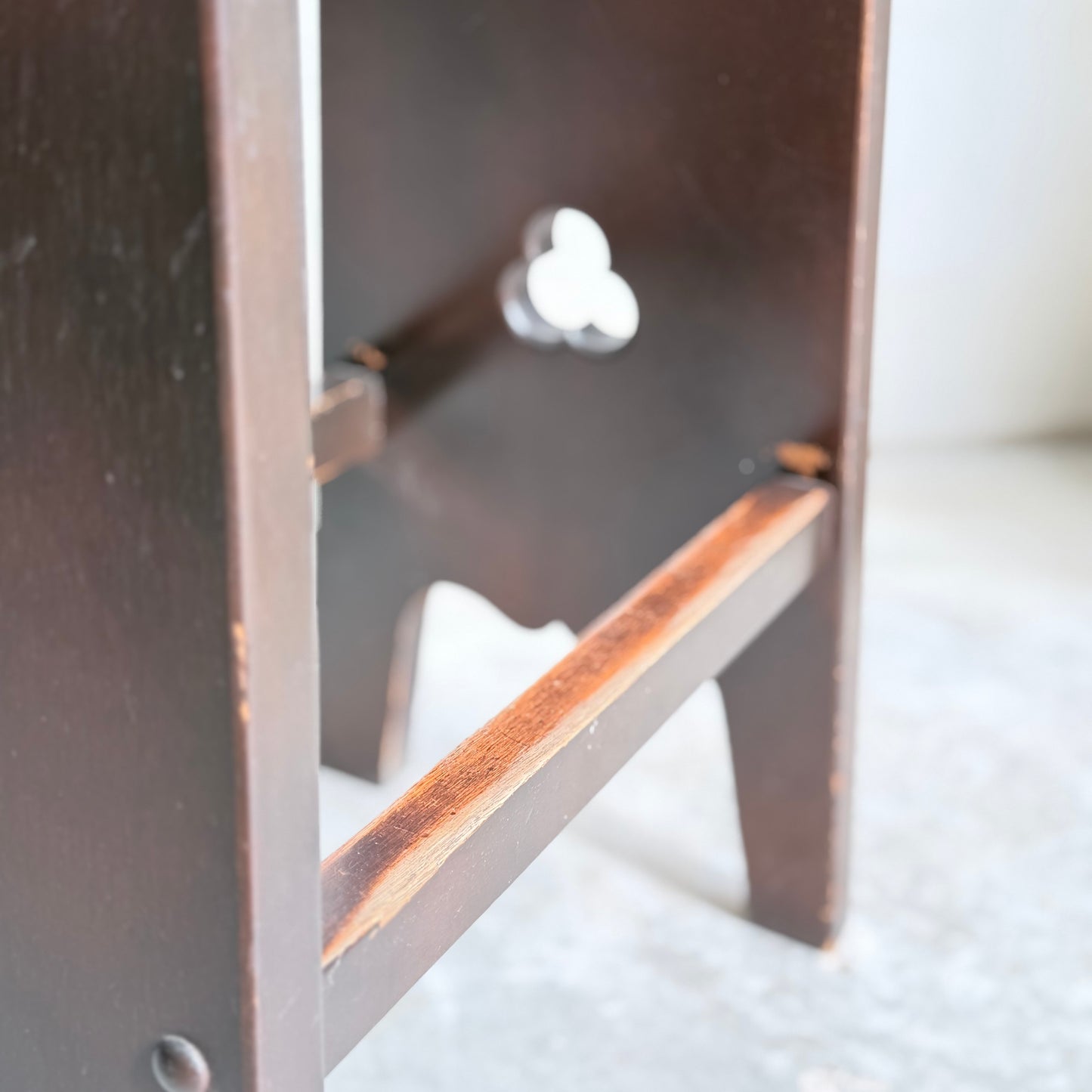 Close-up of a 1970s Australian Mid-Century Modern Spanish Revival Davis stool from the Revive set of 3, featuring dark brown legs and a clover-shaped cutout, highlighting the craftsmanship on a light, textured surface.