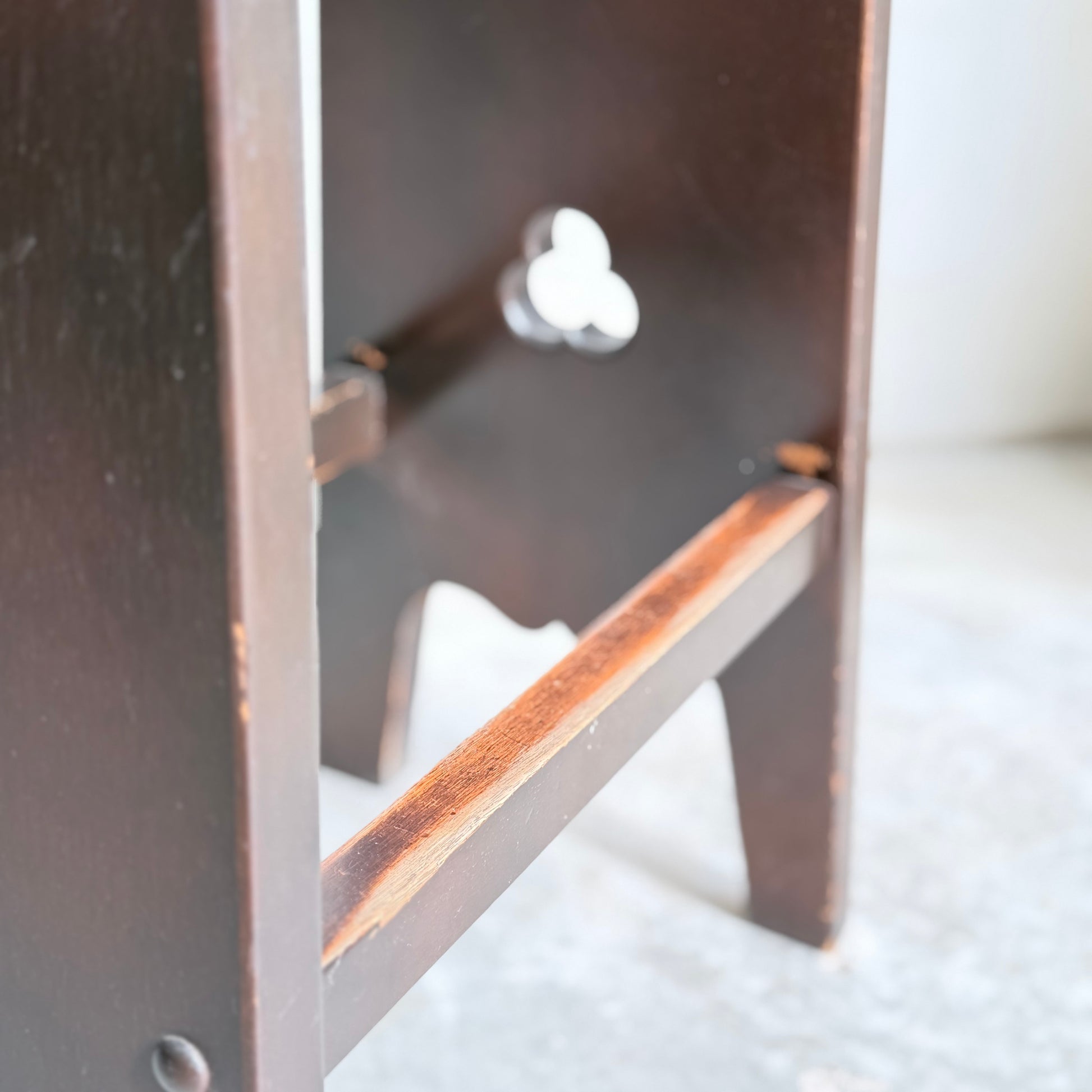 Close-up of a 1970s Australian Mid-Century Modern Spanish Revival Davis stool from the Revive set of 3, featuring dark brown legs and a clover-shaped cutout, highlighting the craftsmanship on a light, textured surface.