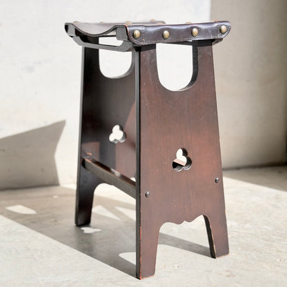 A set of three 1970s Australian Mid-Century Modern Spanish Revival Davis stools (Revive) with clover cutouts and leather seats fastened by metal rivets, shown on a sunlit concrete floor.